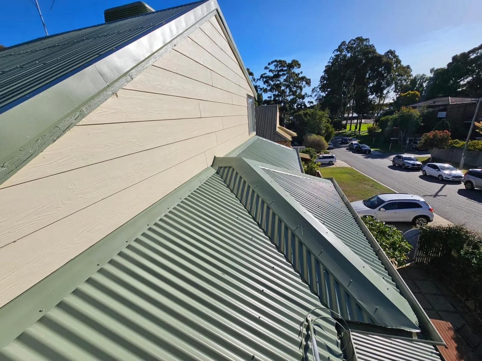 Ridge and valley of a finished green Colorbond metal roof above a quiet suburban street