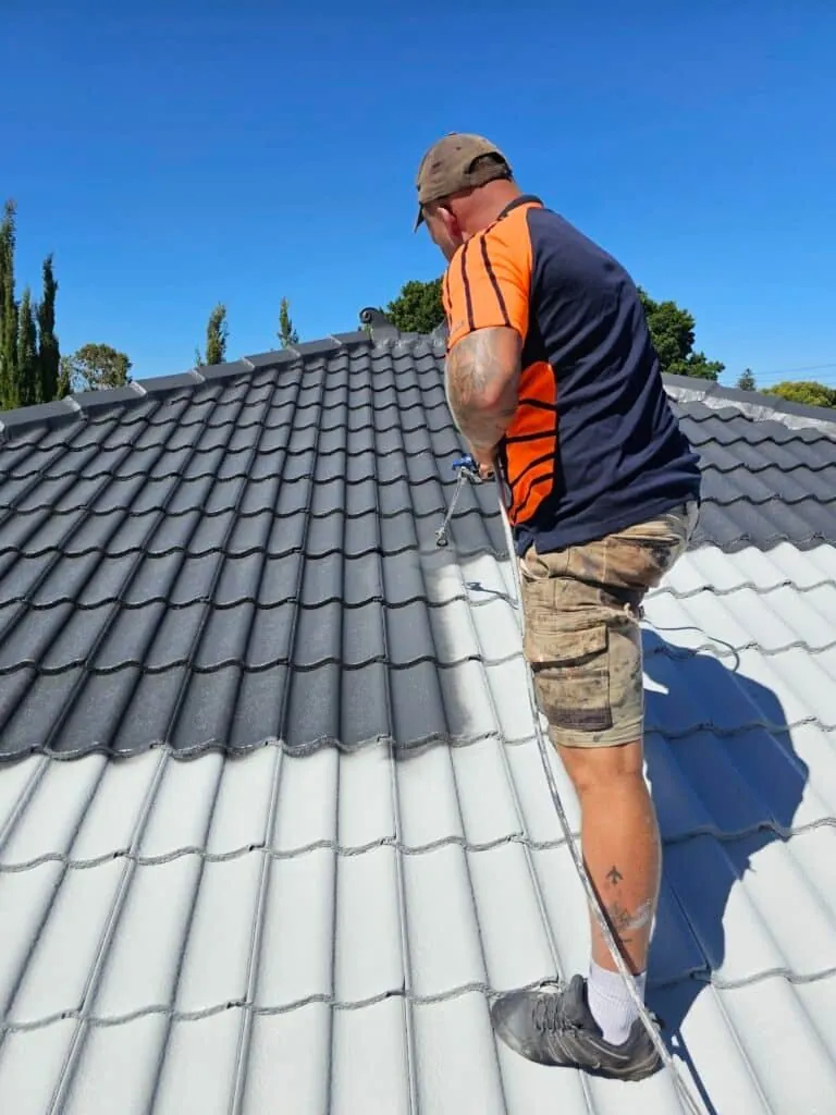 Roofer applying coating along the tiles of a charcoal roof on a clear day