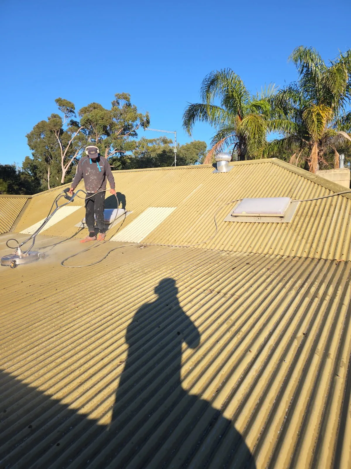 Roofer in safety gear spray applying primer across the corrugated Colorbond sheeting