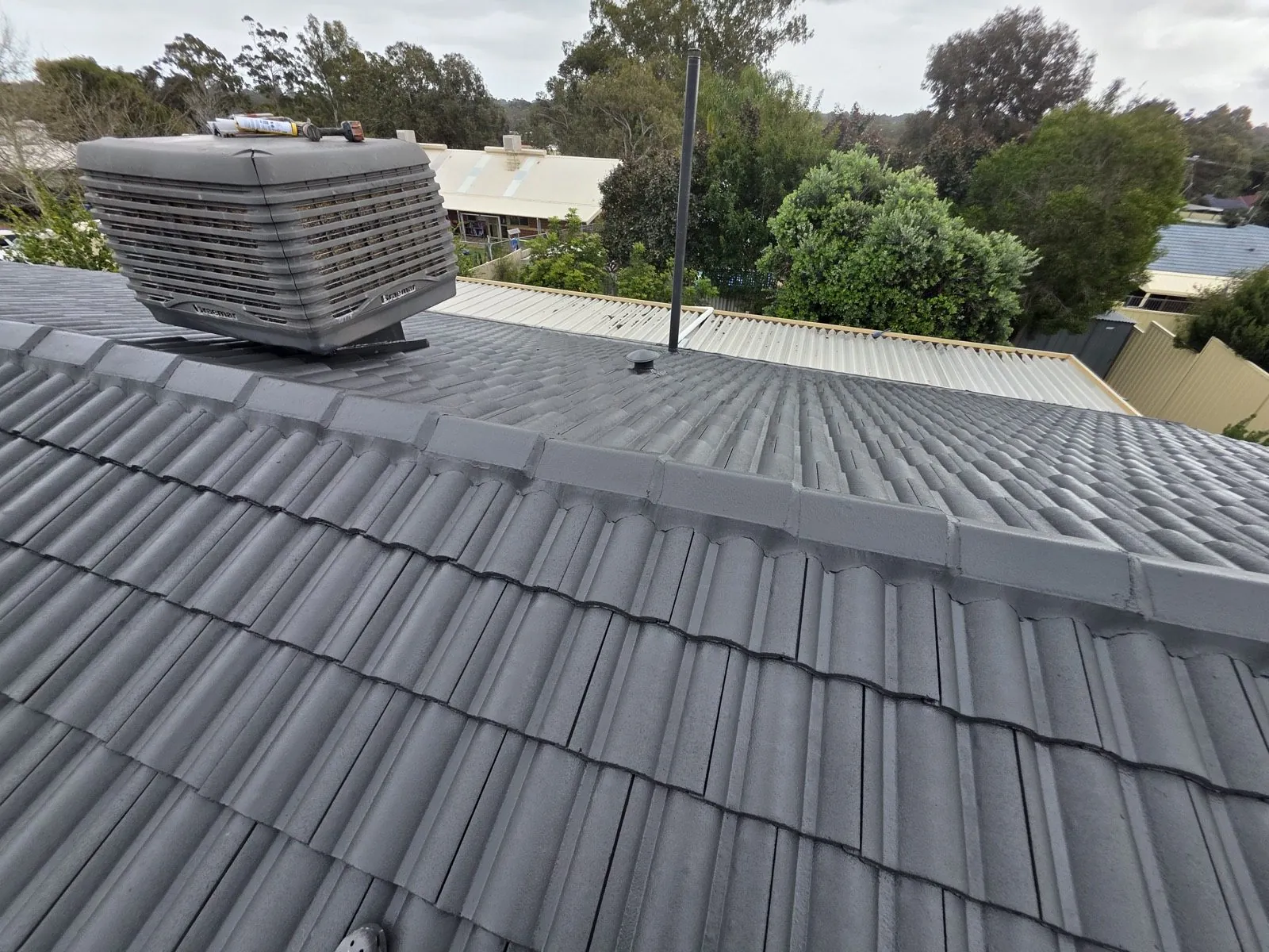 Finished charcoal tile roof seen along the ridge, fresh pointing running the full capping line, evaporative unit and flue in place