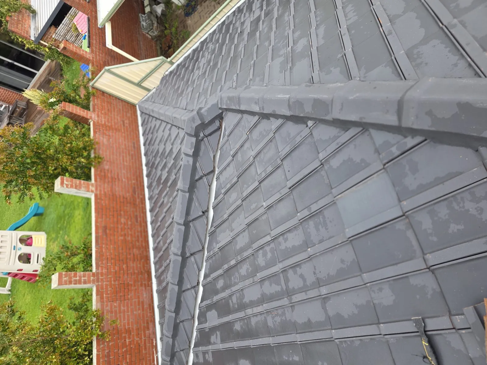 Hip and valley junction of a cleaned tile roof seen from above, brick wall and garden below
